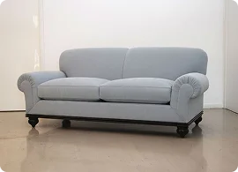 Light blue upholstered sofa with rolled arms and dark wooden legs