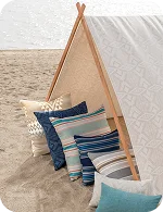 A canvas tent on the beach with colorful patterned pillows in blues and cream