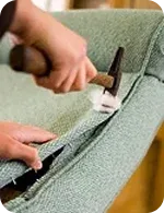 A person uses a hammer to secure fabric on a green upholstered chair