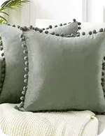 Two soft, light green decorative pillows with pom-pom trim